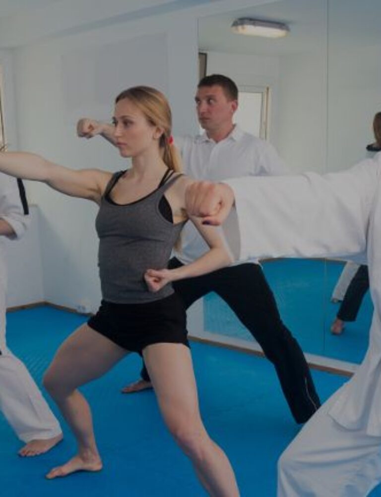 A diverse group of adults practicing punches in a martial arts class