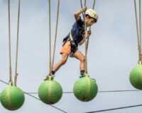 Child in a helmet balancing across suspended green obstacle balls
