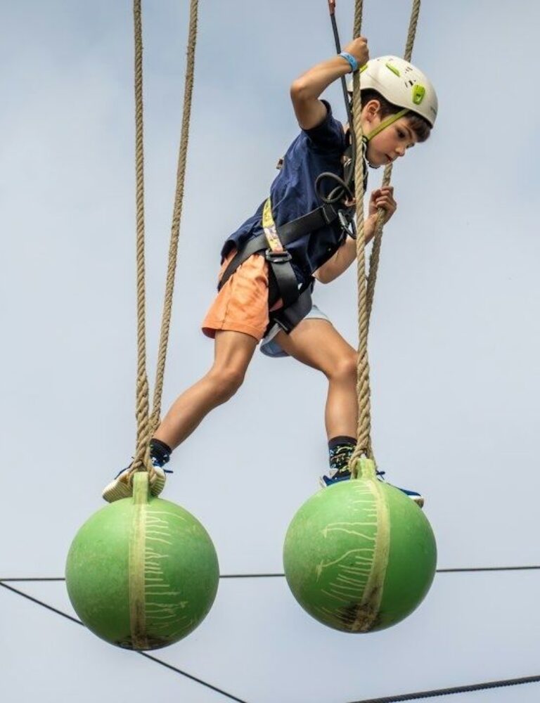 Child in a helmet balancing across suspended green obstacle balls