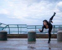Person practicing a high leg extension on a wet riverside promenade