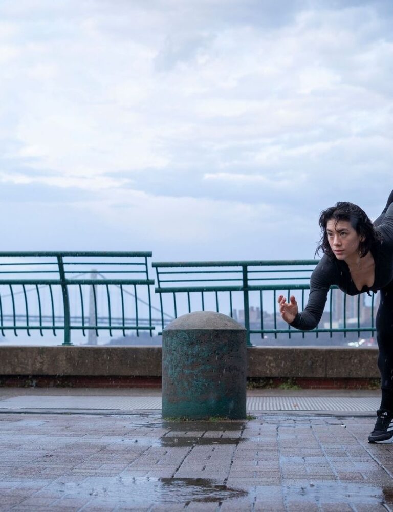 Person practicing a high leg extension on a wet riverside promenade