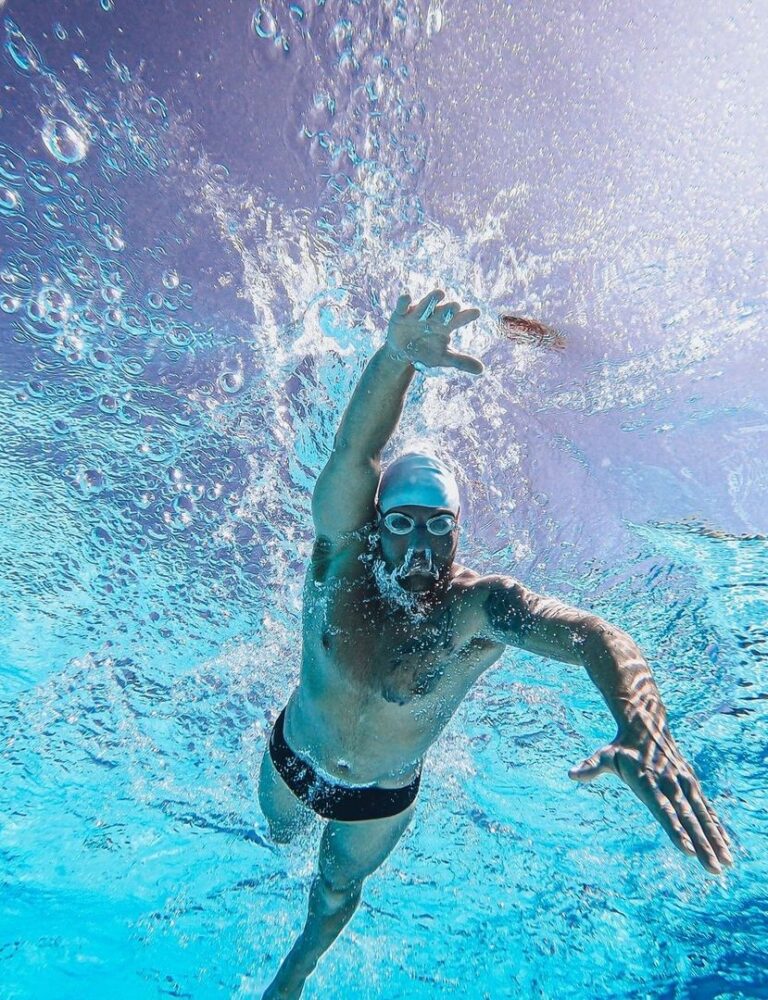 Swimmer moving underwater while wearing goggles and creating bubbles