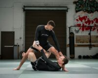 Two martial artists demonstrate a controlled ground movement on a training mat