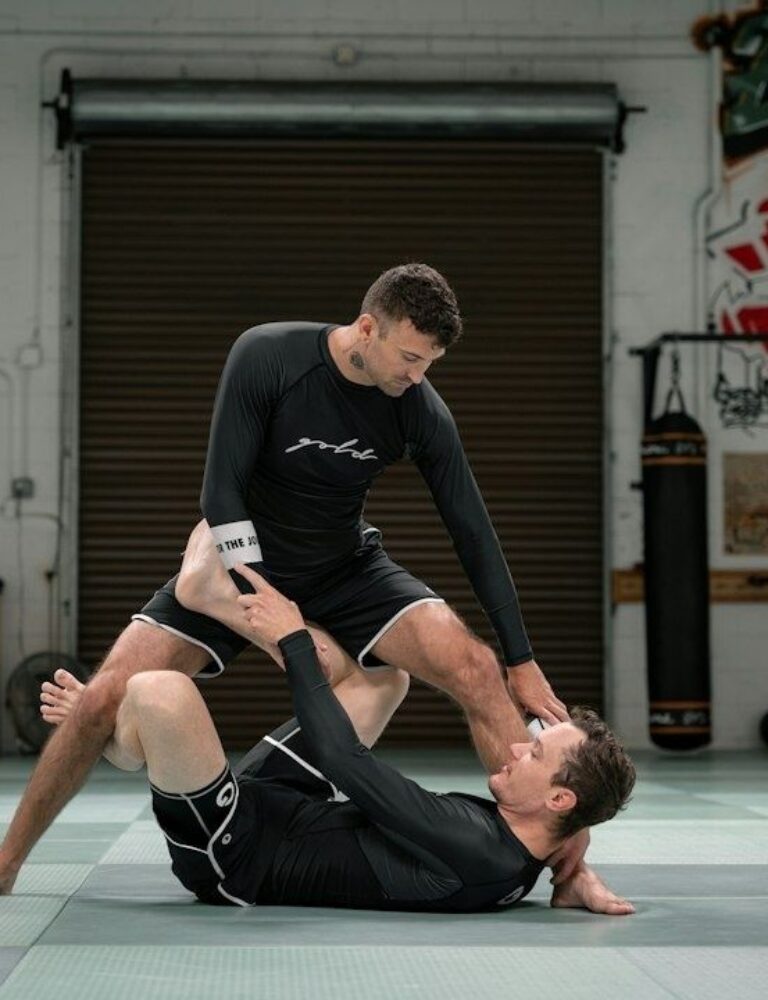 Two martial artists demonstrate a controlled ground movement on a training mat